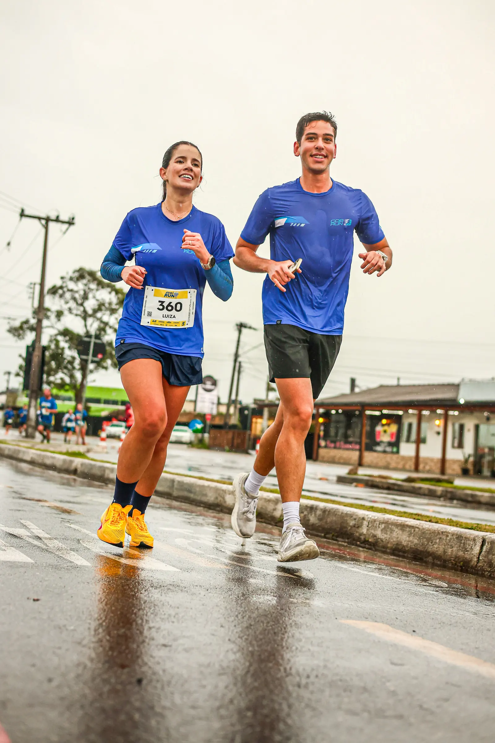 Dois atletas da COB Run correndo juntos sob chuva em uma prova de rua