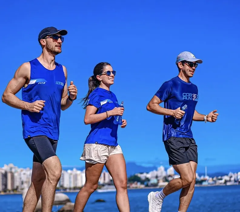 Três atletas da COB Run correndo lado a lado na orla